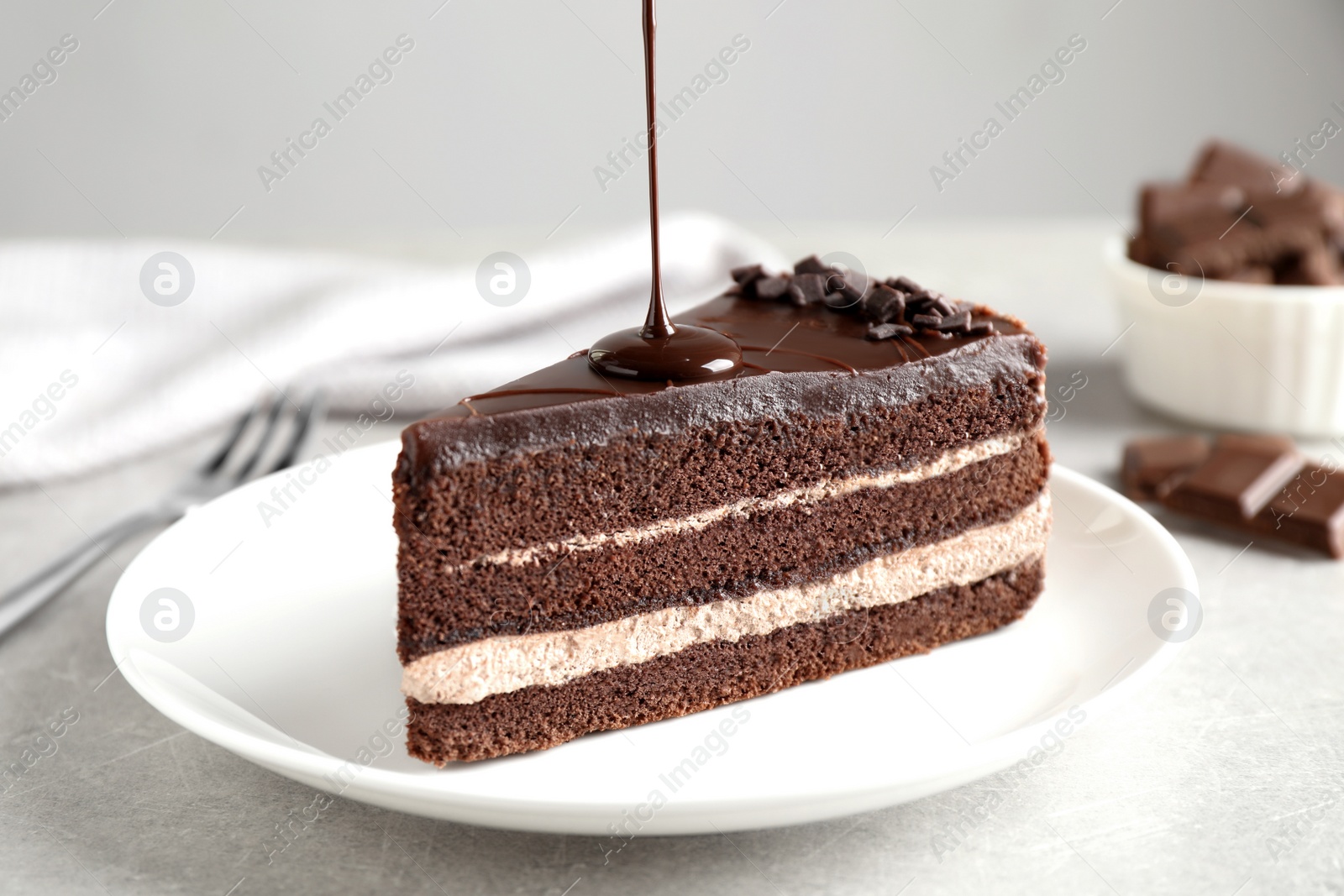 Photo of Pouring chocolate sauce onto delicious fresh cake on light table, closeup