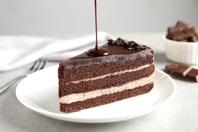 Pouring chocolate sauce onto delicious fresh cake on light table, closeup