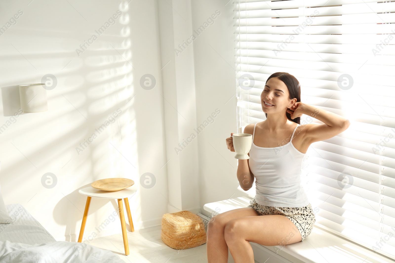 Photo of Young woman with cup of tea near window. Lazy morning