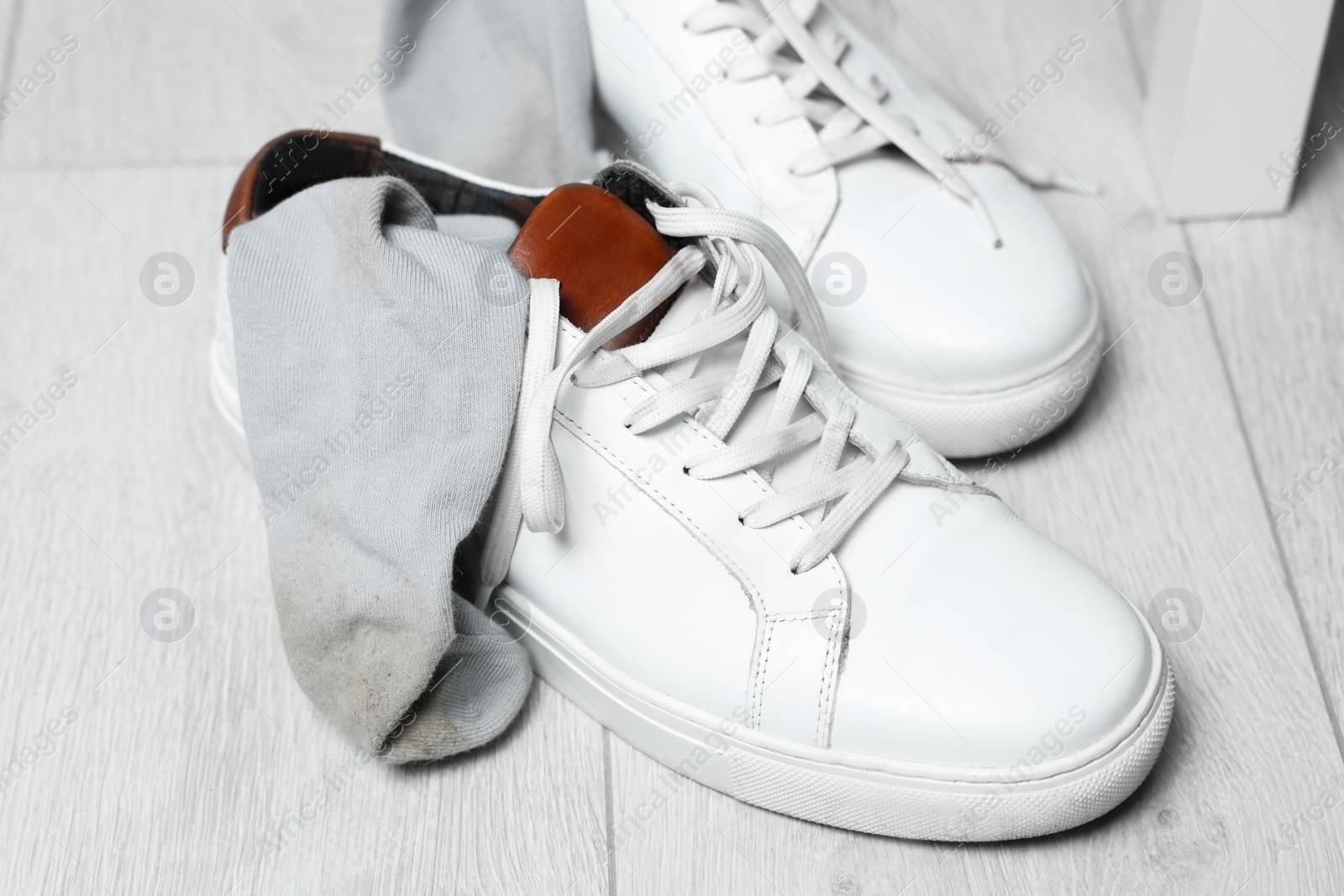 Photo of Sneakers with dirty socks on white wooden floor indoors