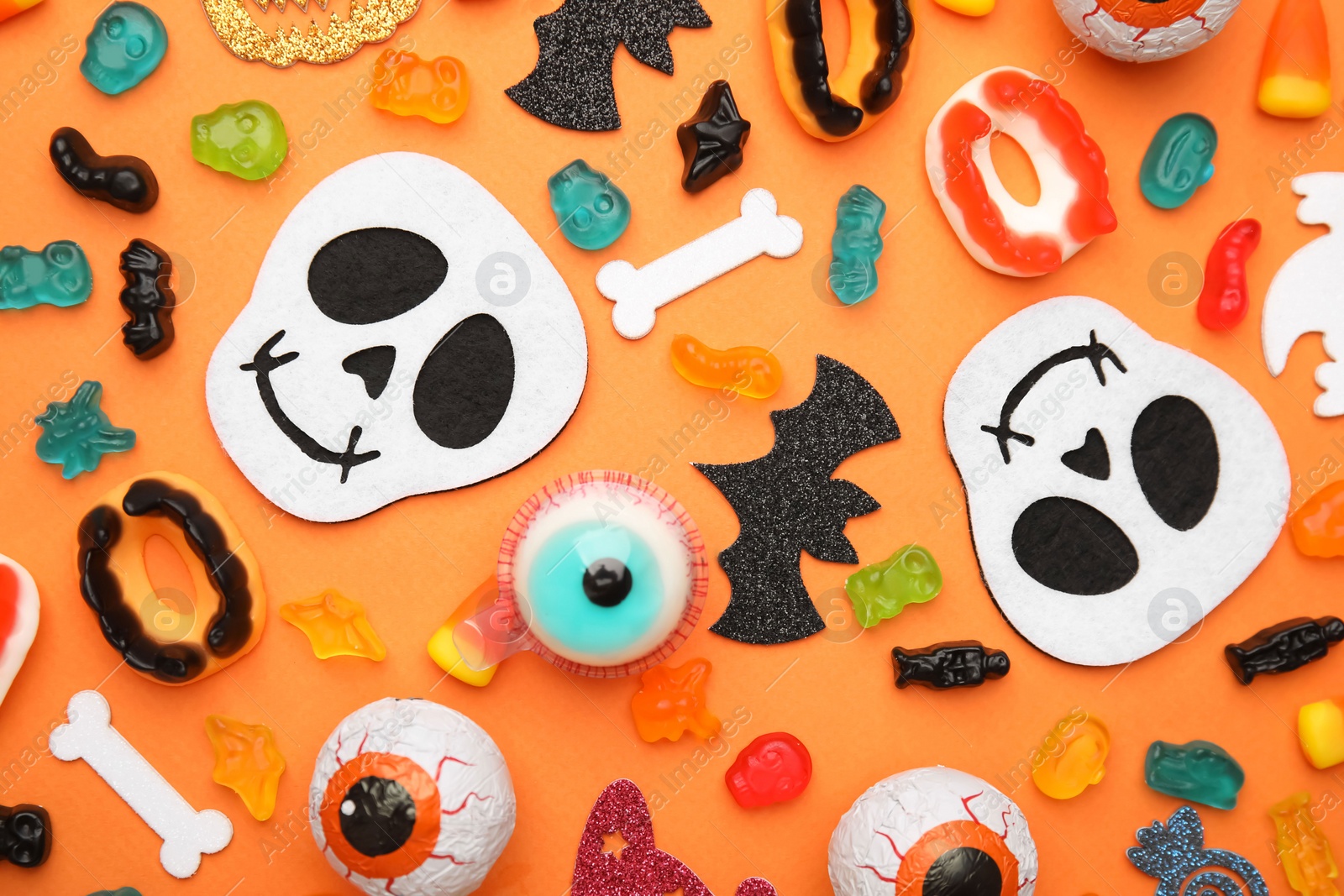 Photo of Tasty candies and Halloween decorations on orange background, flat lay