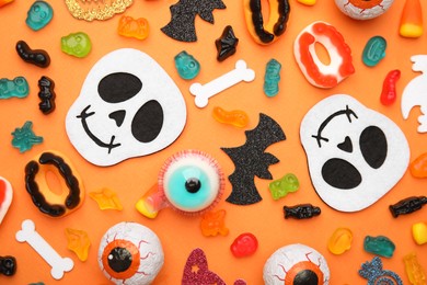 Tasty candies and Halloween decorations on orange background, flat lay