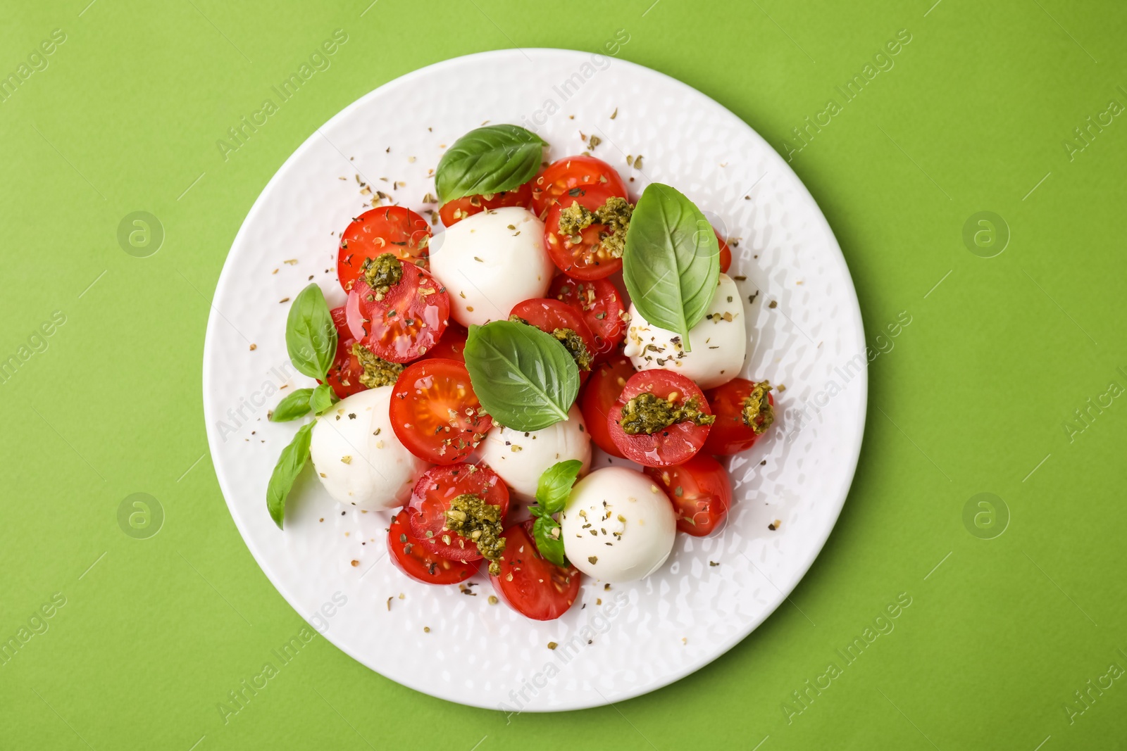Photo of Tasty salad Caprese with tomatoes, mozzarella balls and basil on green background, top view