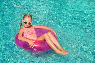 Photo of Cute little girl with inflatable ring in pool on sunny day. space for text