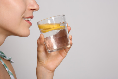 Photo of Young woman drinking lemon water on light background, closeup