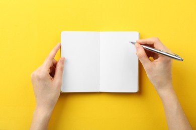 Woman writing in notebook on yellow background, top view