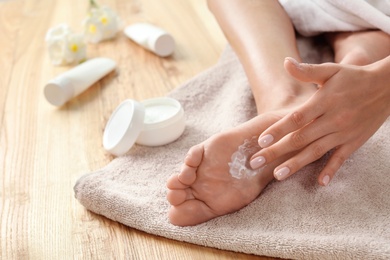 Photo of Woman applying foot cream on towel, closeup. Spa treatment