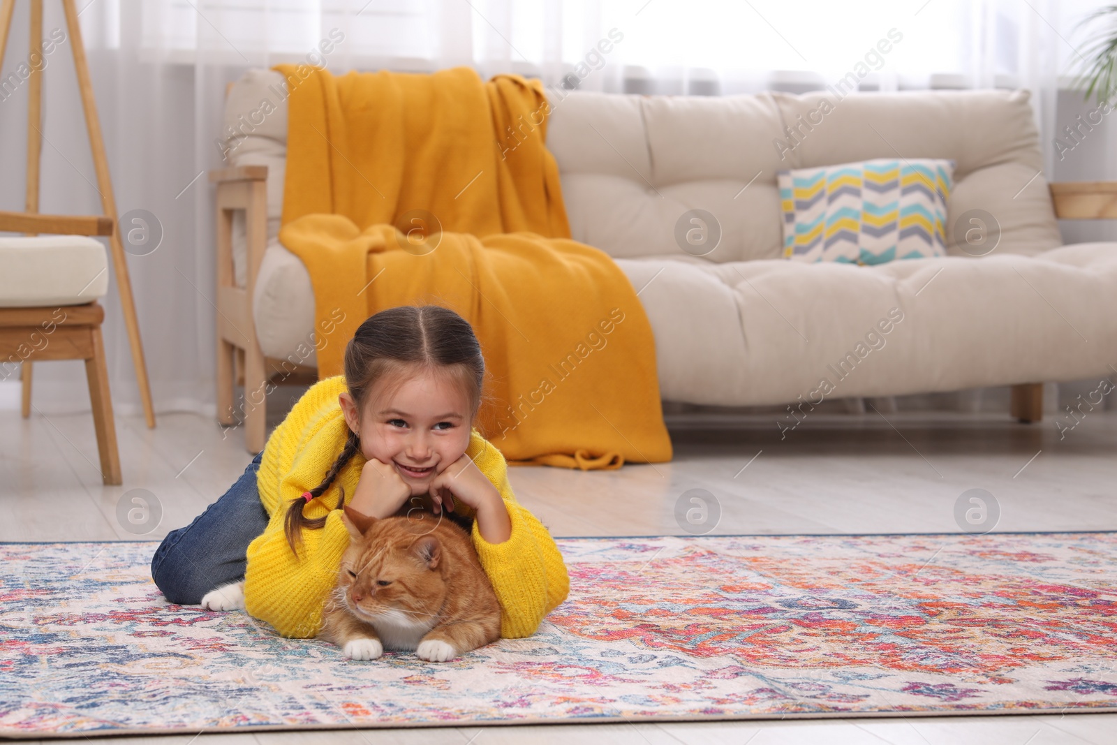 Photo of Happy little girl and cute ginger cat on carpet at home, space for text