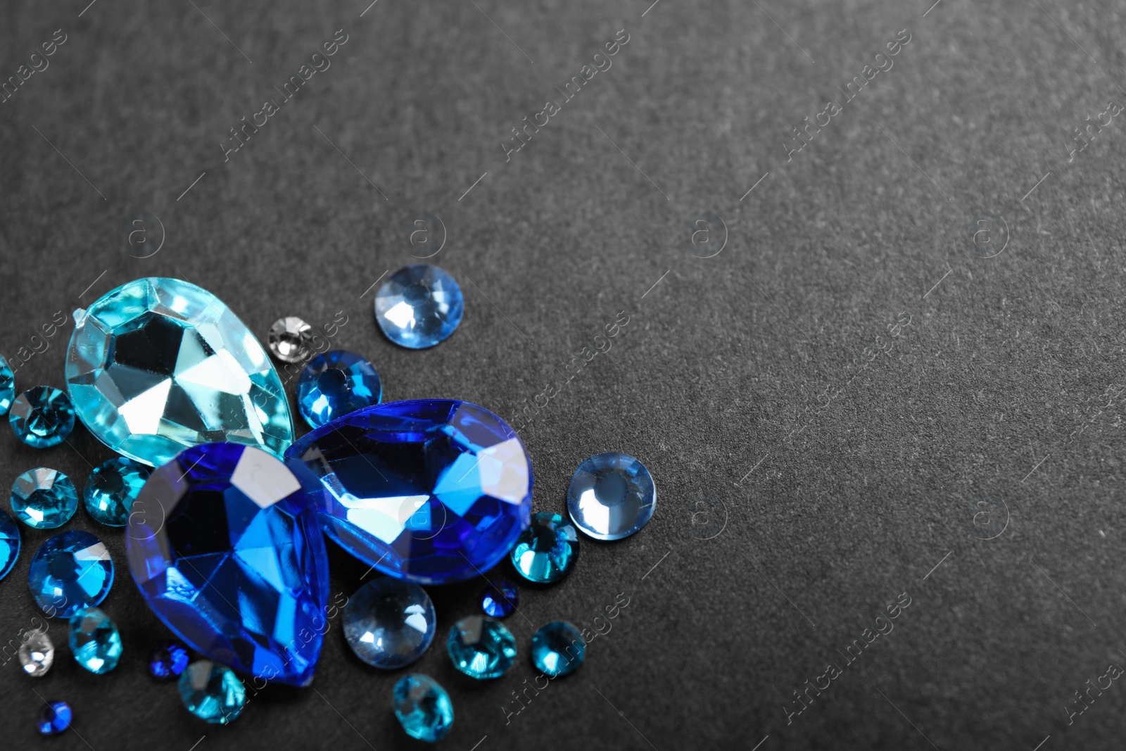 Photo of Pile of different beautiful gemstones on black background. Space for text