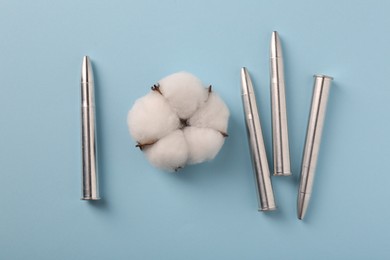 Bullets and beautiful cotton flower on light blue background, flat lay