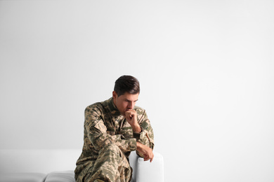 Stressed military officer sitting on sofa against white background. Space for text