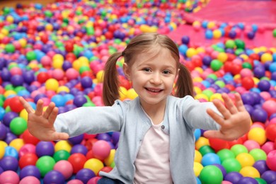 Photo of Happy little girl sitting on colorful balls in ball pit
