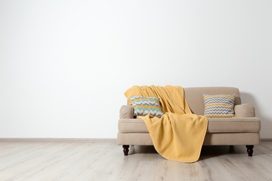 Photo of Minimalist living room interior with sofa, pillows and plaid near light wall. Space for text