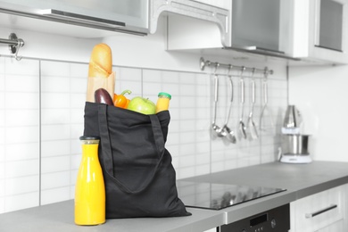 Photo of Textile shopping bag full of vegetables with juice and baguette on countertop in kitchen. Space for text