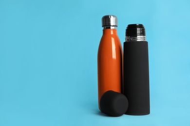 Stylish thermo bottles on light blue background, space for text