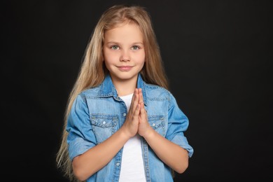 Photo of Girl with clasped hands praying on black background