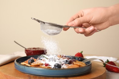 Woman pouring powdered sugar onto cereal pancakes with berries at table, closeup