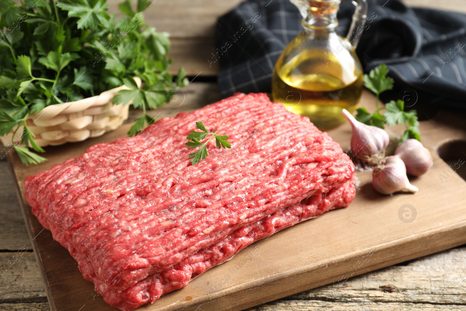 Photo of Raw ground meat, garlic, oil and parsley on wooden table