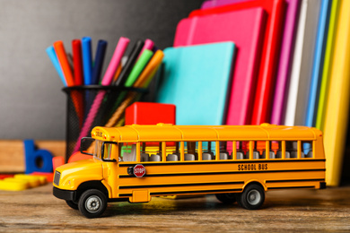 Photo of School bus model and stationery on wooden table. Transport for students