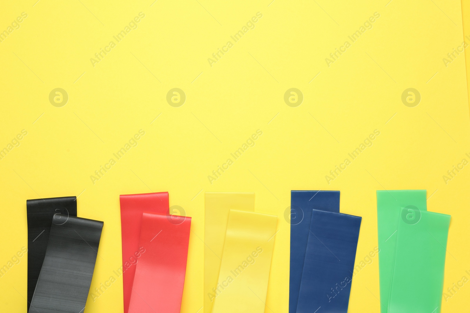 Photo of Set of fitness elastic bands on yellow background, flat lay. Space for text