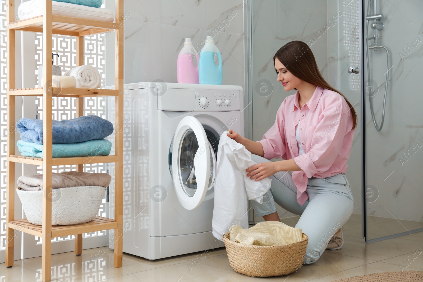 Photo of Young woman with clothes near washing machine in bathroom. Laundry day