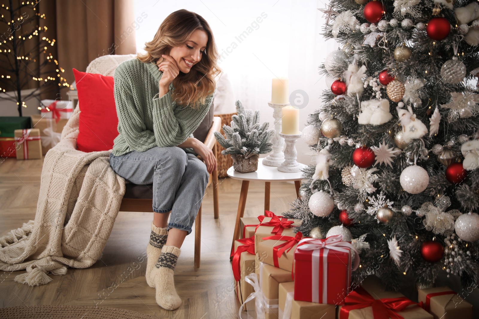 Photo of Young woman in armchair near Christmas tree at home