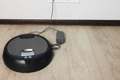 Photo of Robotic vacuum cleaner charging on wooden floor near white wall, space for text