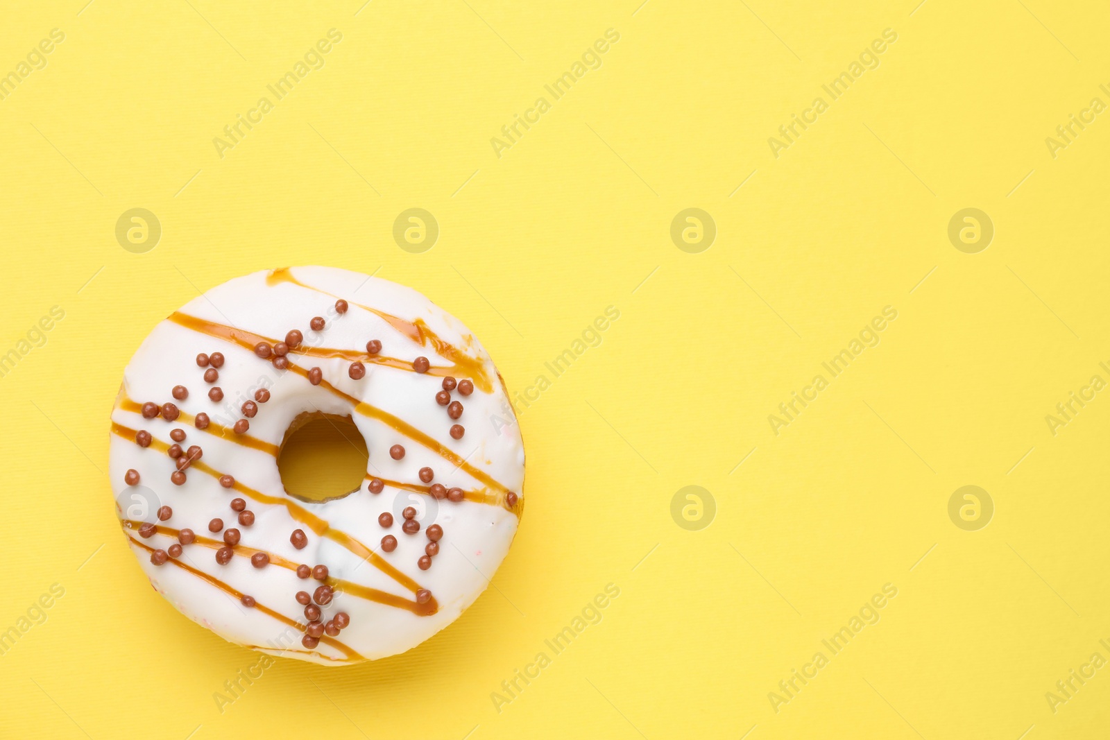 Photo of Tasty glazed donut decorated with sprinkles and caramel on yellow background, top view. Space for text