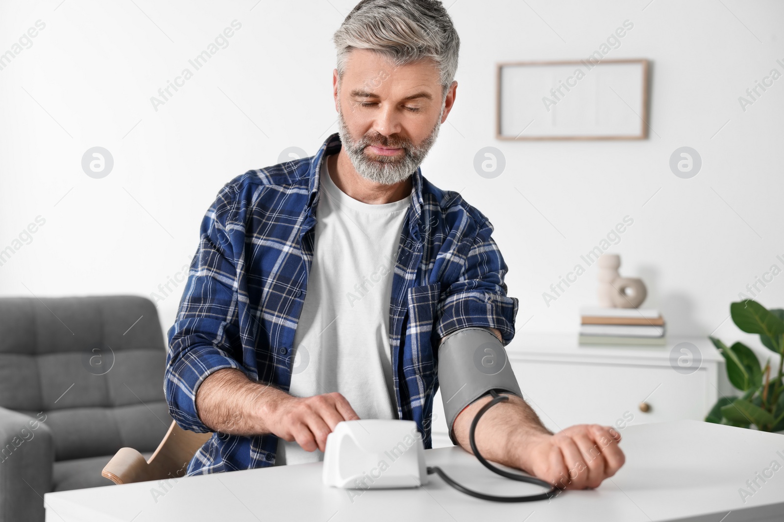 Photo of Man measuring blood pressure at table indoors