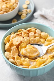 Photo of Spoon in bowl with tasty cornflakes and milk on table, closeup