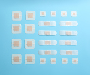 Photo of Different types of sticking plasters on light blue background, flat lay