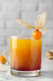 Delicious cocktail decorated with physalis fruit on white marble table