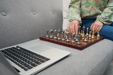 Photo of Woman playing chess with partner through online video chat on sofa, closeup