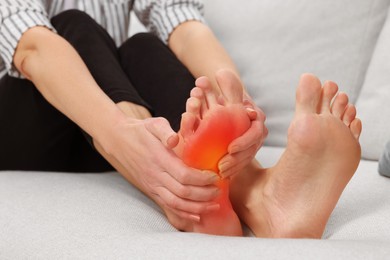 Image of Arthritis symptoms. Woman suffering from foot pain on sofa indoors, closeup