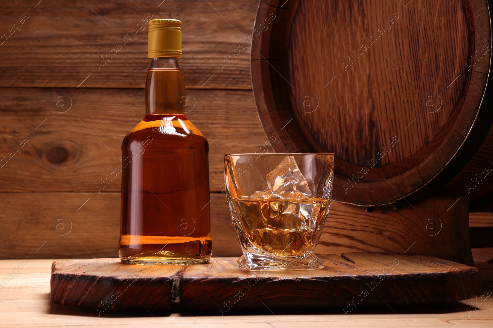 Photo of Whiskey with ice cubes in glass, bottle and barrel on wooden table