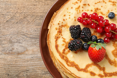 Delicious thin pancakes with berries on wooden table, closeup