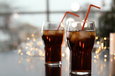 Photo of Glasses of cold cola against blurred fairy lights. Space for text