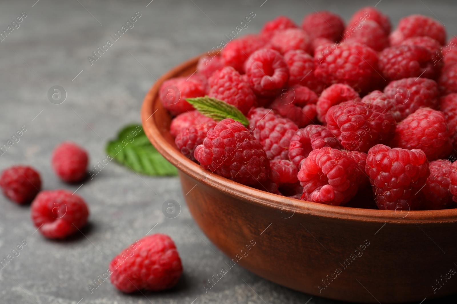 Photo of Bowl with delicious ripe raspberries on stone surface, closeup. Space for text