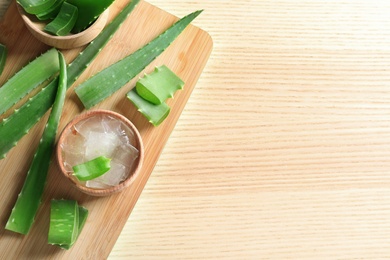 Flat lay composition with bowl of peeled aloe vera, green leaves and space for text on wooden table