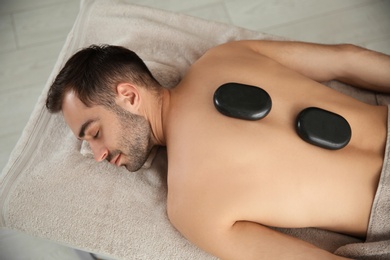 Photo of Handsome man receiving hot stone massage in spa salon, top view