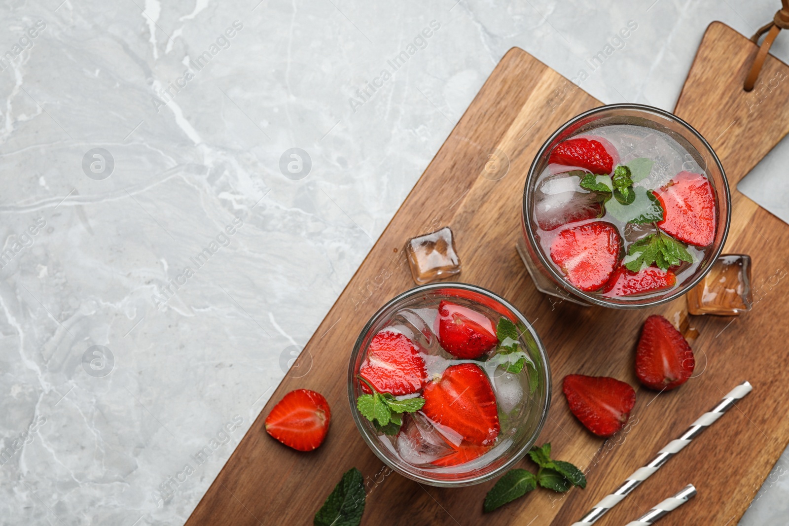 Photo of Glasses of refreshing drink with strawberry and mint on grey stone table, flat lay. Space for text