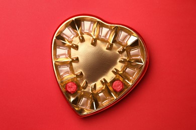 Photo of Partially empty heart shaped box of chocolate candies on red background, top view