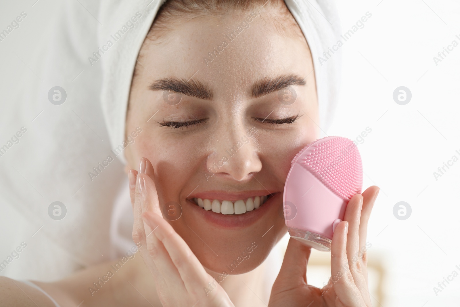 Photo of Washing face. Young woman with cleansing brush on light background, closeup