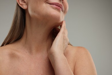 Mature woman touching her neck on grey background, closeup