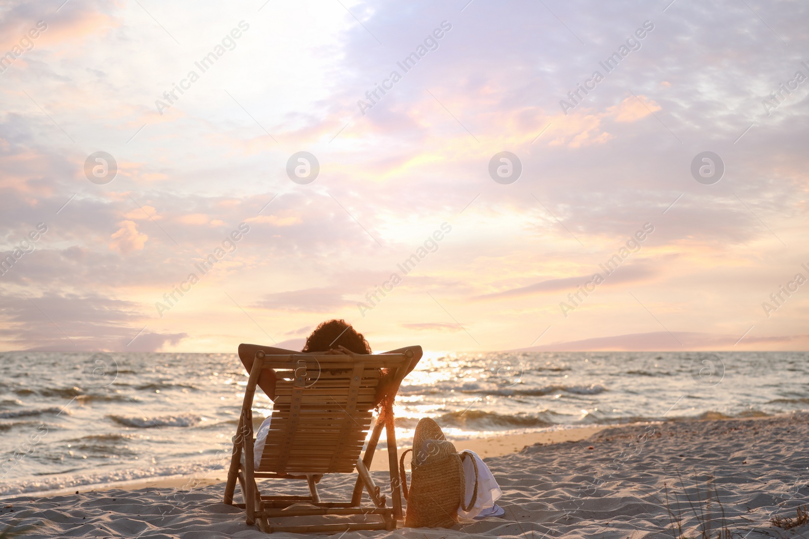 Photo of Woman resting in wooden sunbed on tropical beach at sunset