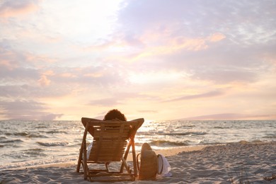 Photo of Woman resting in wooden sunbed on tropical beach at sunset