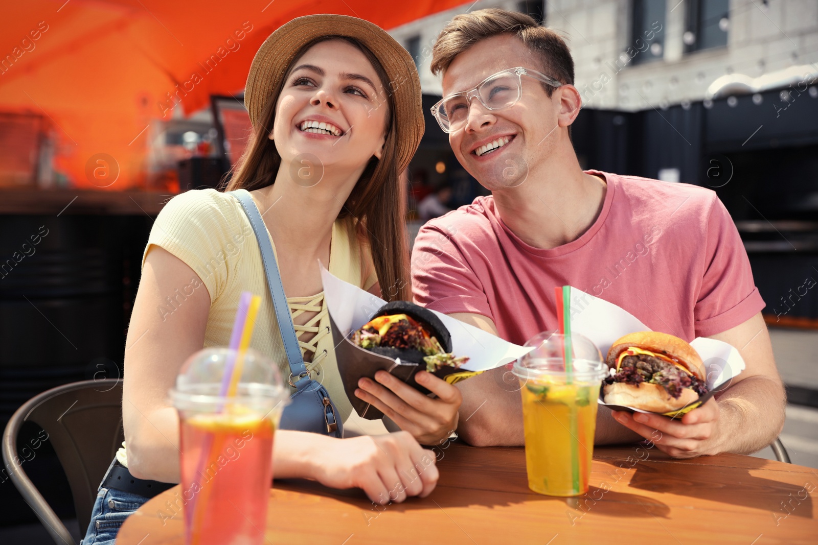 Photo of Young happy couple with burgers in street cafe