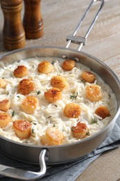 Photo of Delicious scallop pasta in pan on wooden table, closeup