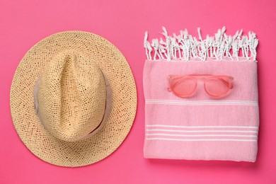 Photo of Stylish straw hat, towel and sunglasses on pink  background, flat lay