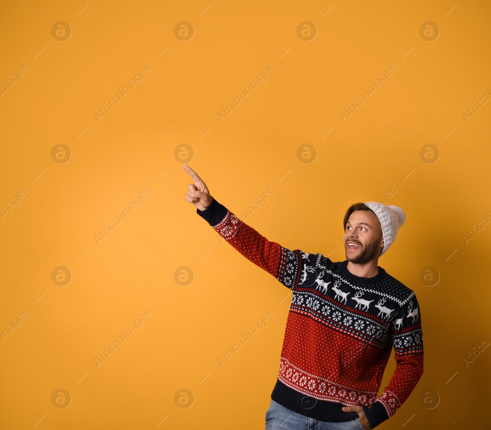Photo of Young man in Christmas sweater and hat on yellow background. Space for text